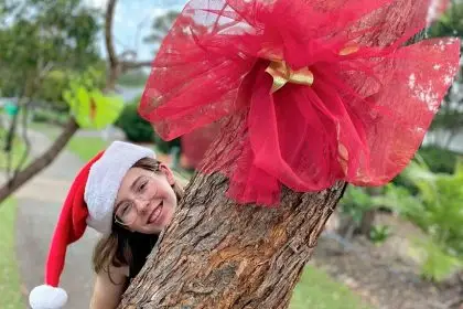 Ada Quinn enjoys the festivity that the Christmas bows in Hardwood Drive bring. The bows were distributed and tied on trees along the road by resident Pamela Jean.